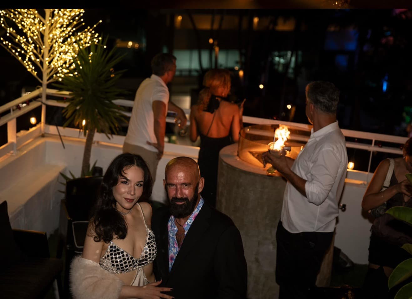 Guests mingling at a rooftop event under warm string lights